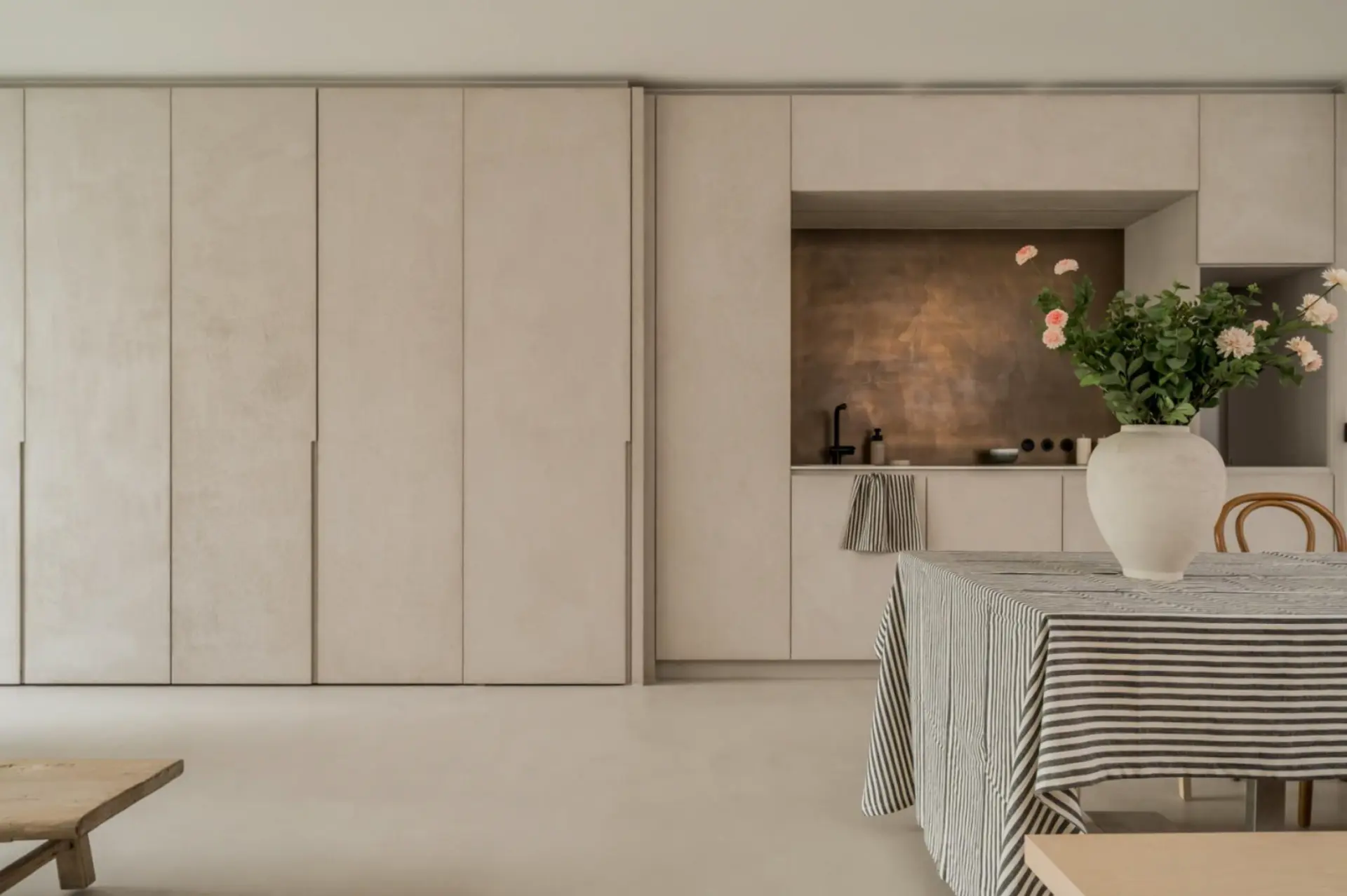 Kitchen and dining area with seamless microcement floors and cabinetry panels and a bronze splashback niche