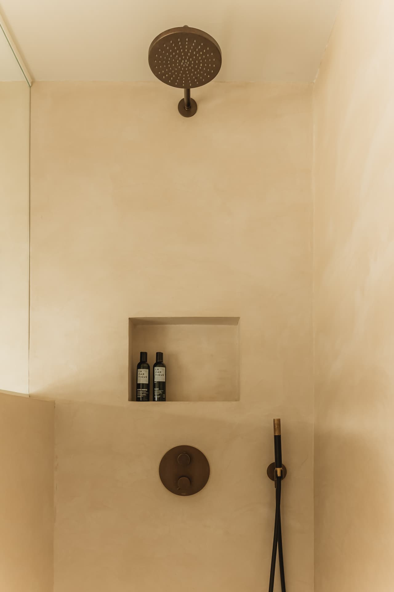 Walk-in shower with a dark rain showerhead and recessed niche in warm cream plaster