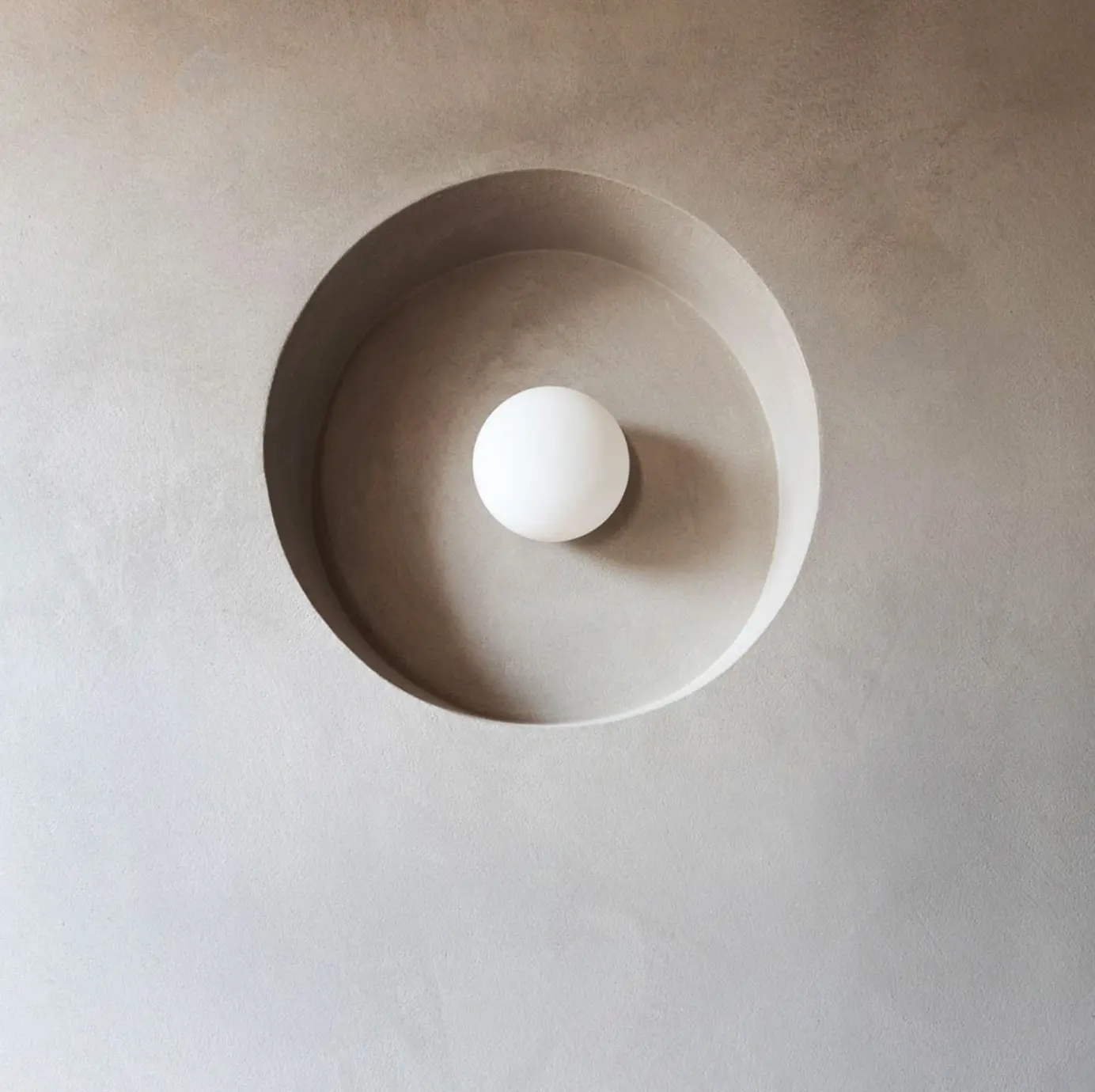 Recessed circular ceiling niche in warm grey plaster around a spherical light