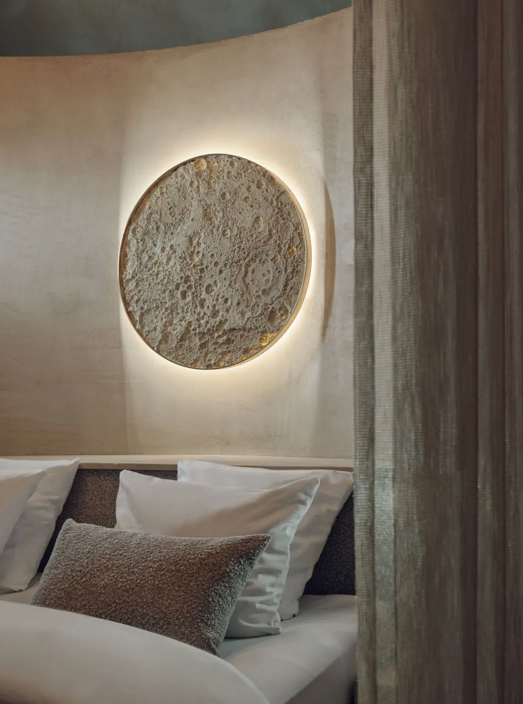 Bedroom with curved warm beige plaster walls and a backlit circular relief artwork