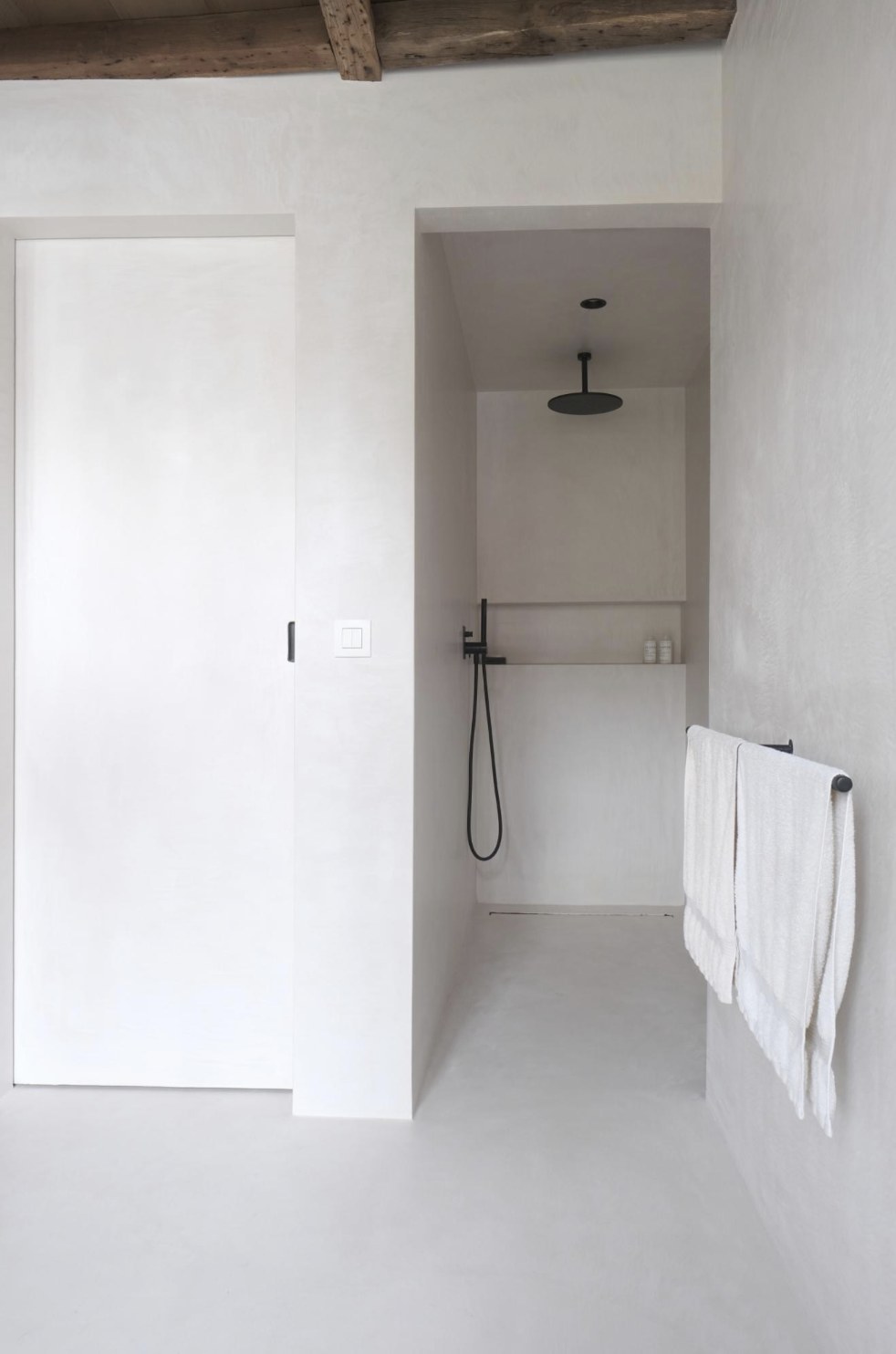 Bathroom with seamless off-white microcement walls, floor and shower enclosure beneath matte black fixtures