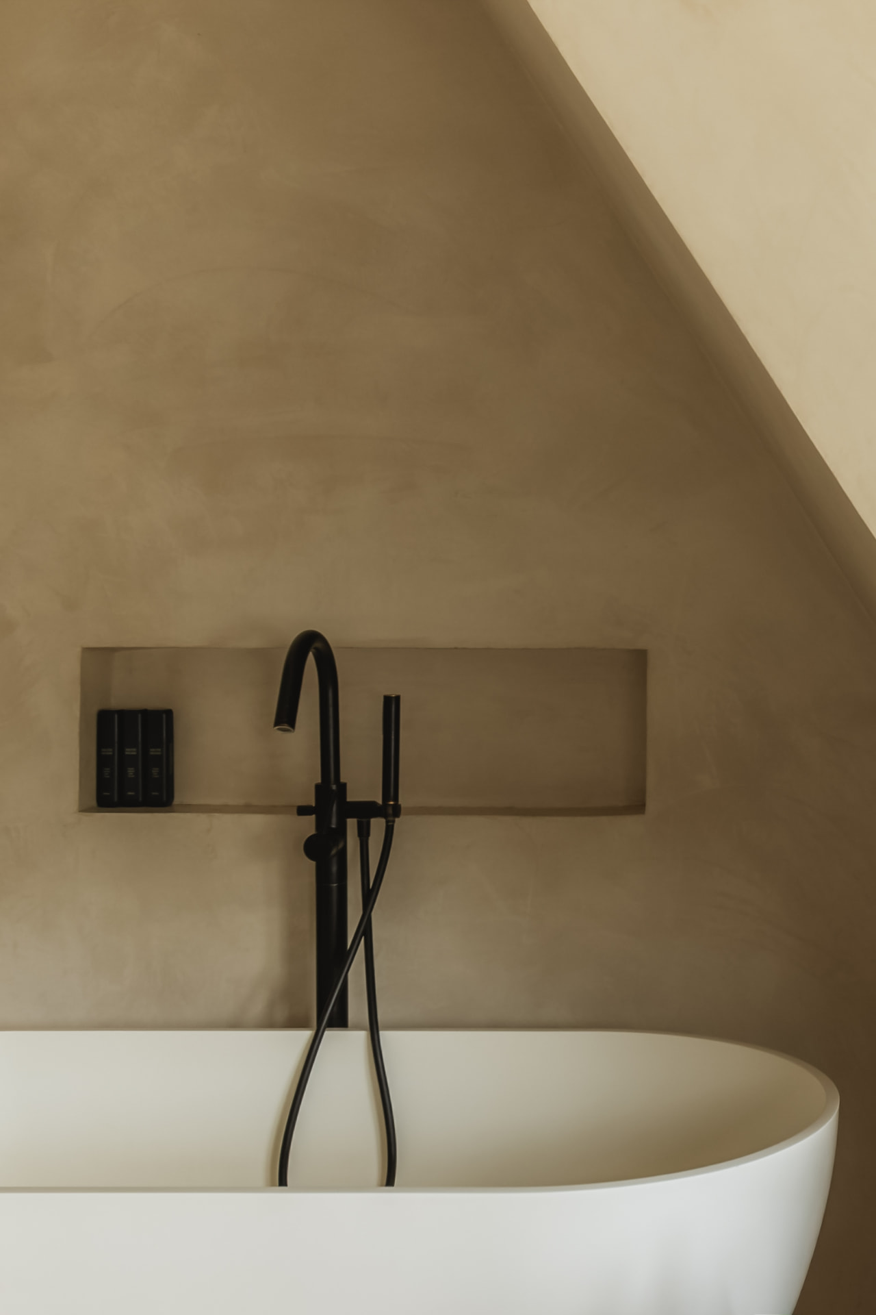 Freestanding oval soaking tub with a matte black floor-mounted filler beneath a sloped plaster ceiling