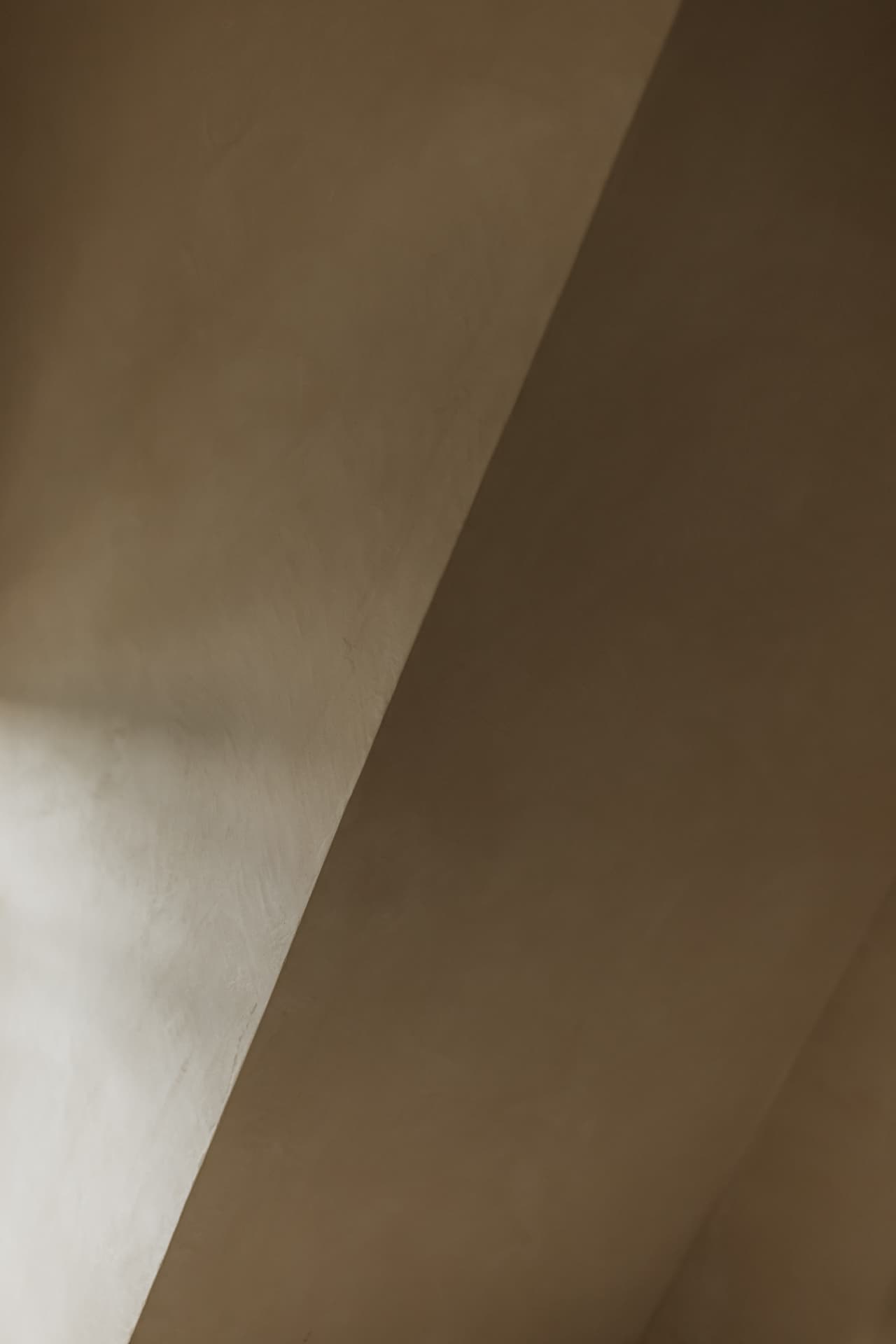 Sloped plaster walls and ceiling meeting at a crisp diagonal in warm taupe