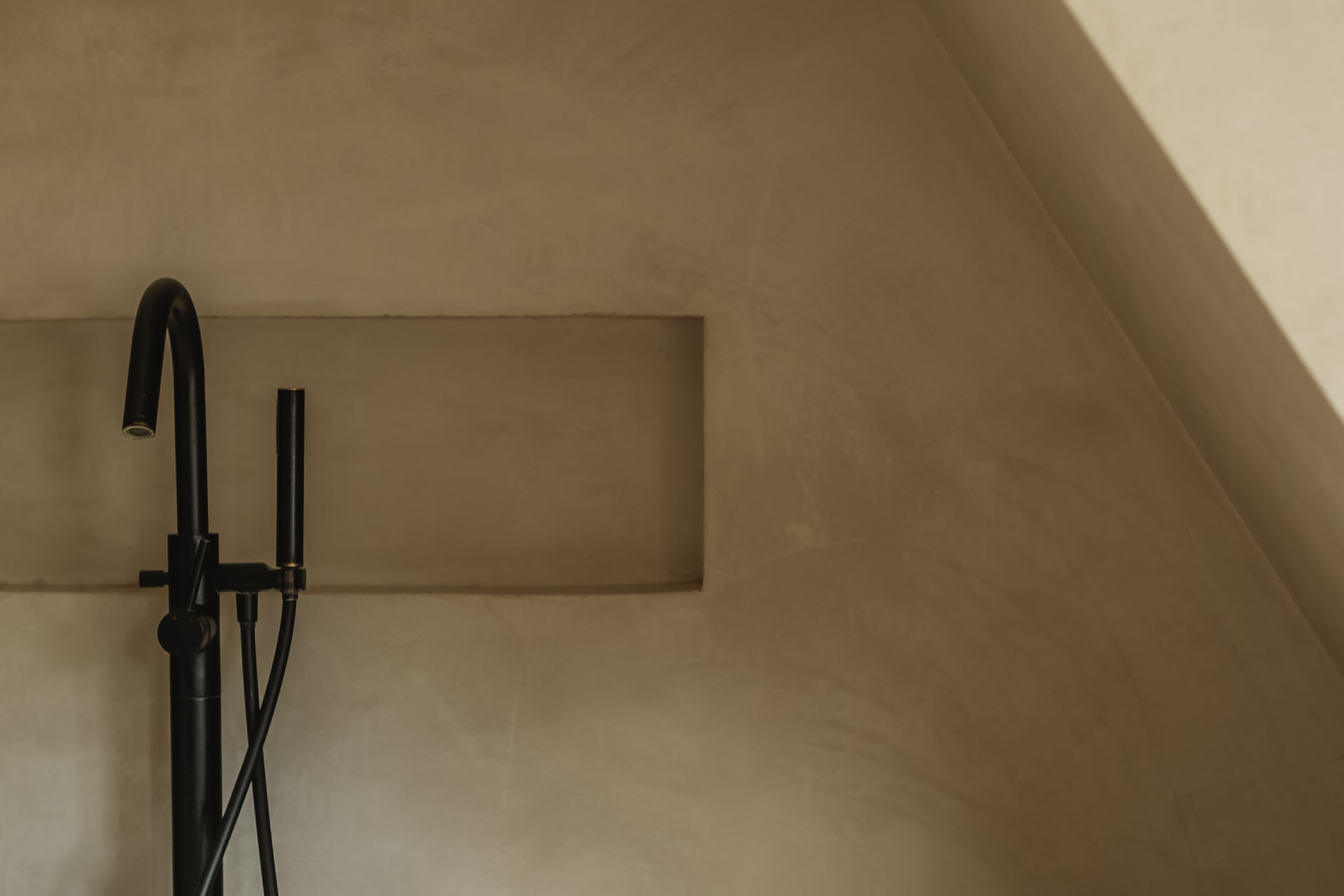 Matte black faucet against a textured mineral wall with a recessed niche
