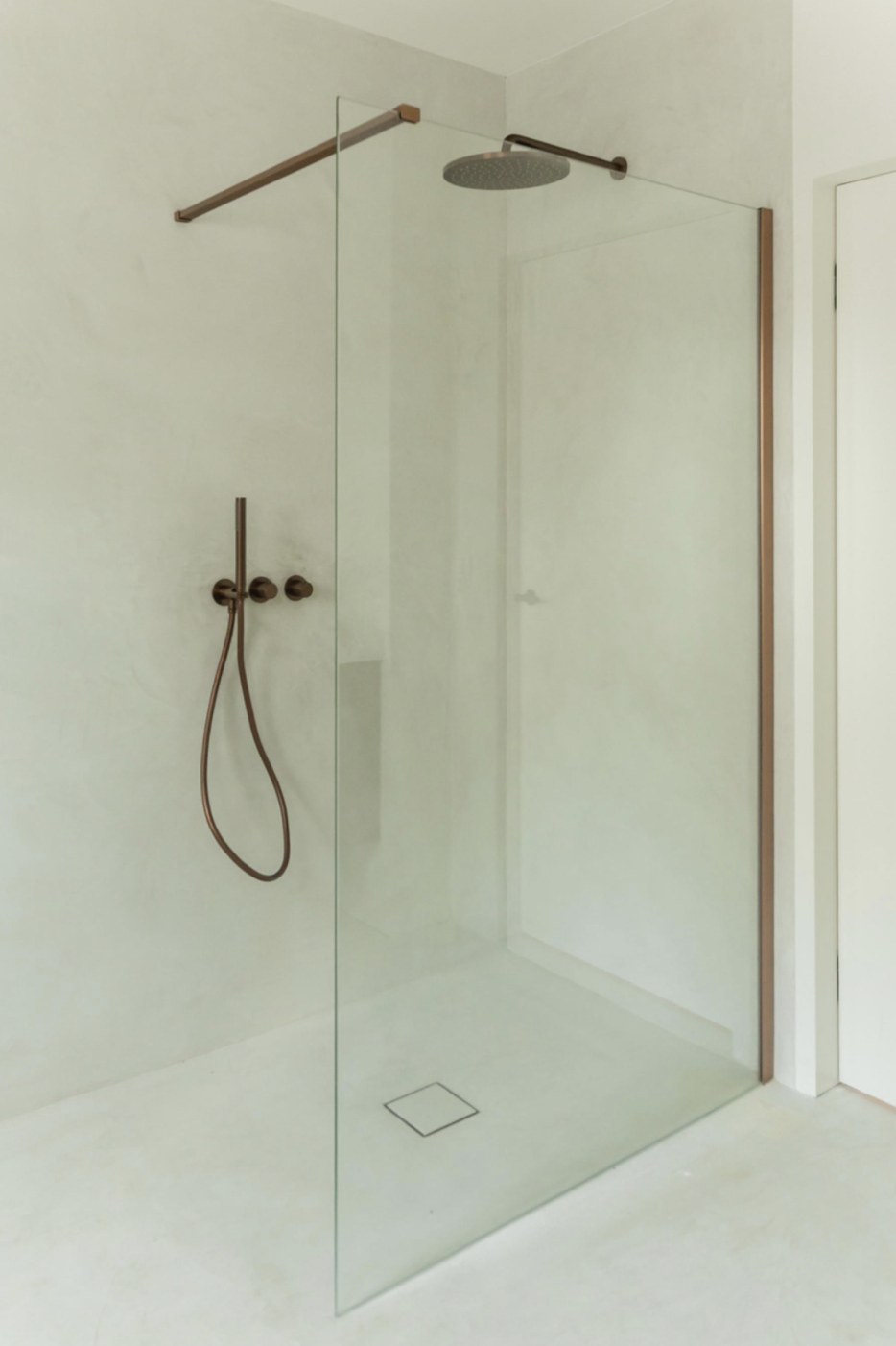 Walk-in shower in pale off-white microcement with dark bronze hardware
