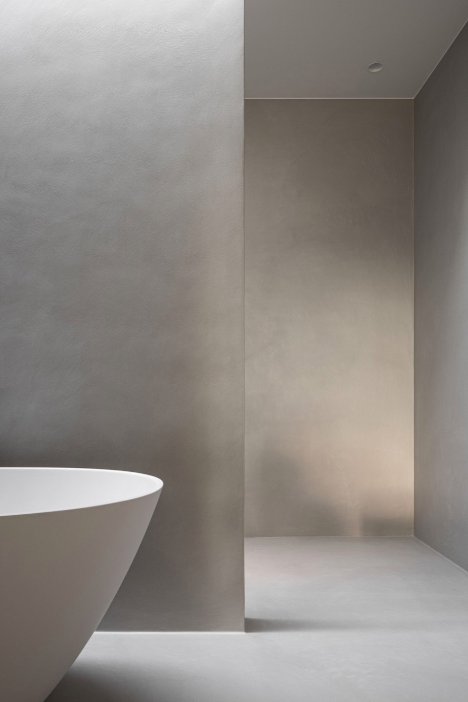 Warm taupe-grey microcement walls beside a curved freestanding bathtub