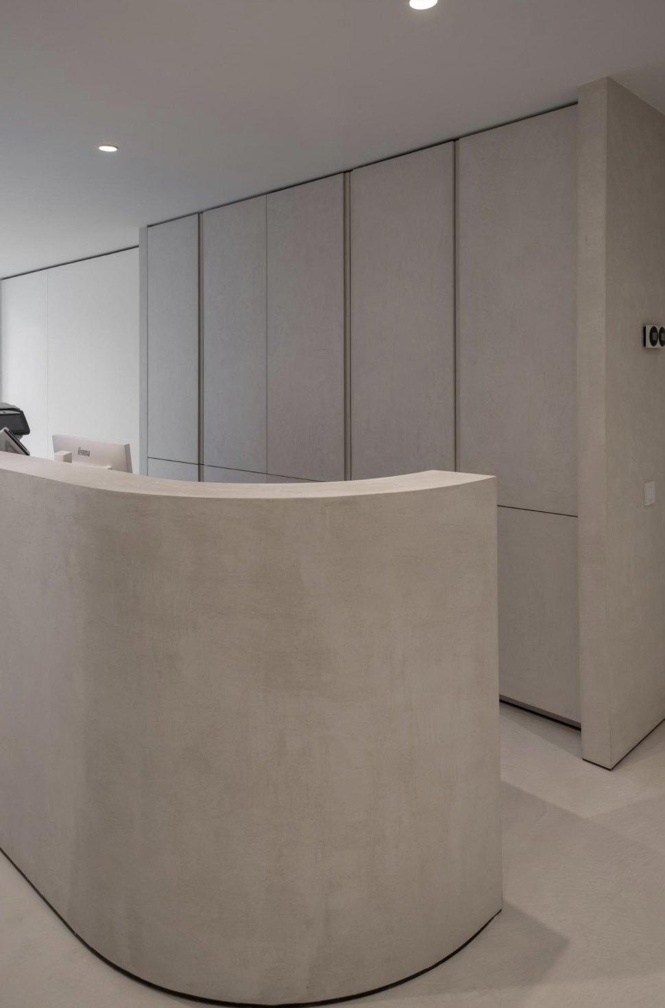 Curved reception desk in seamless grey microcement with matching panelling and floor