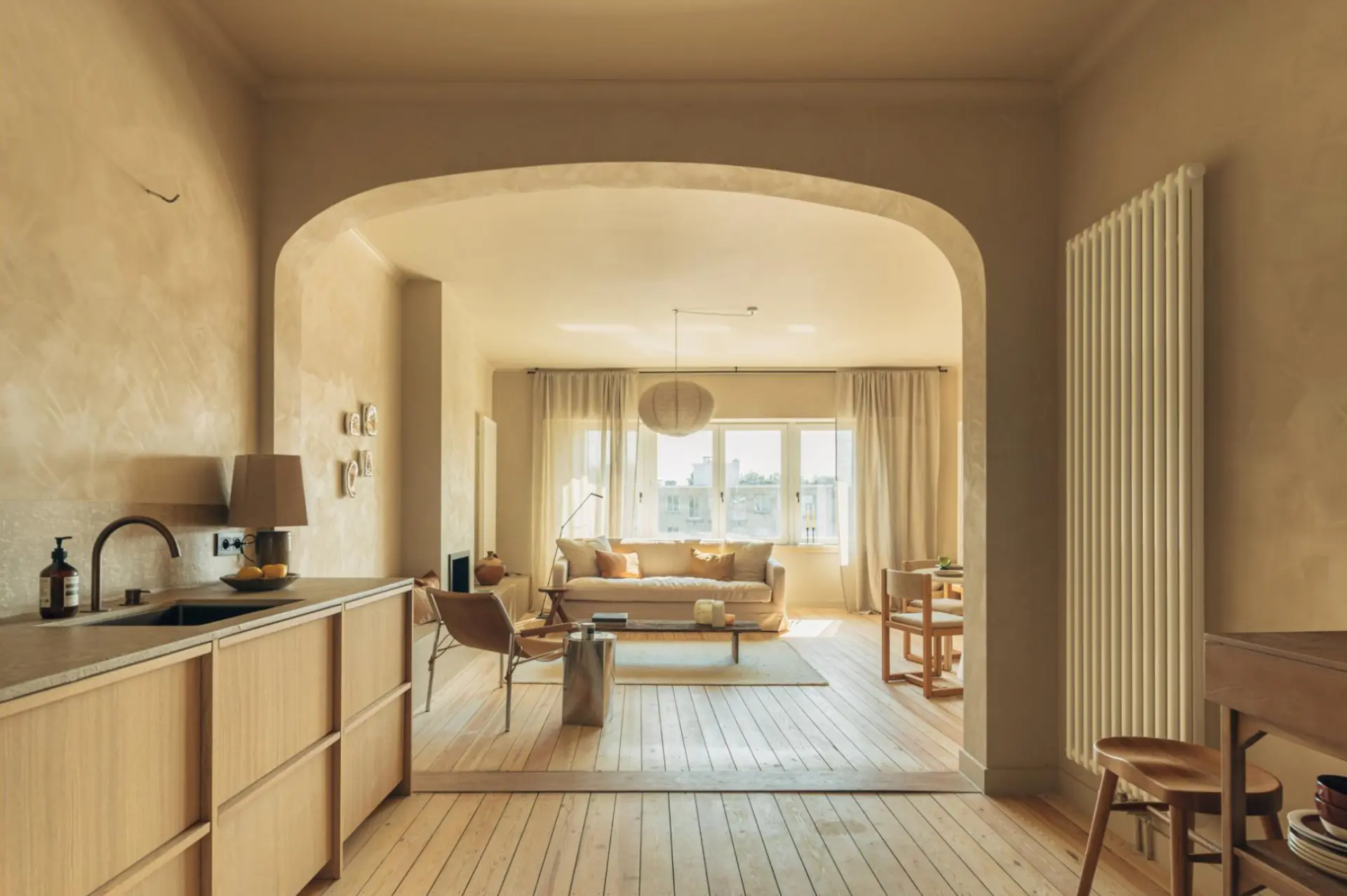 Open-plan kitchen and living area with warm beige mineral plaster walls and archway